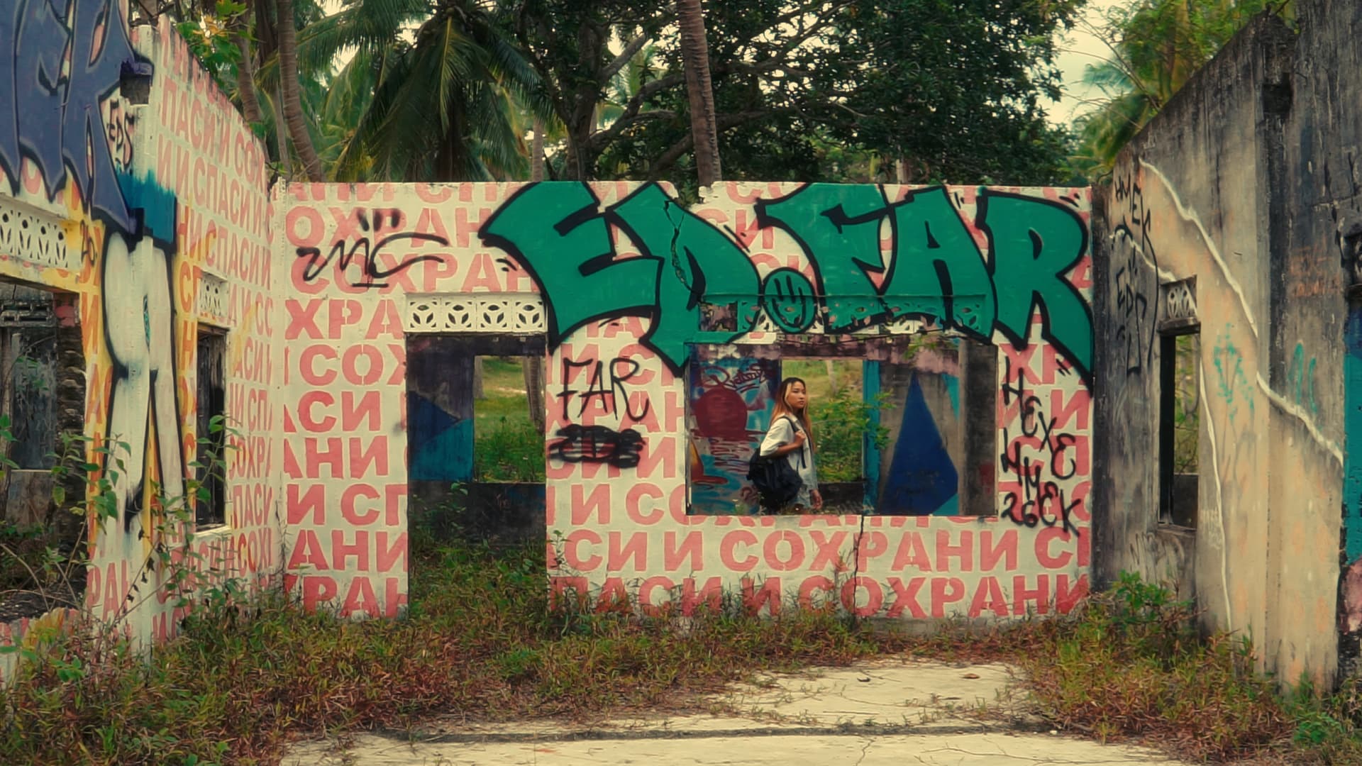 Woman with backpack stands inside a roofless building covered in vibrant graffiti and Cyrillic text.